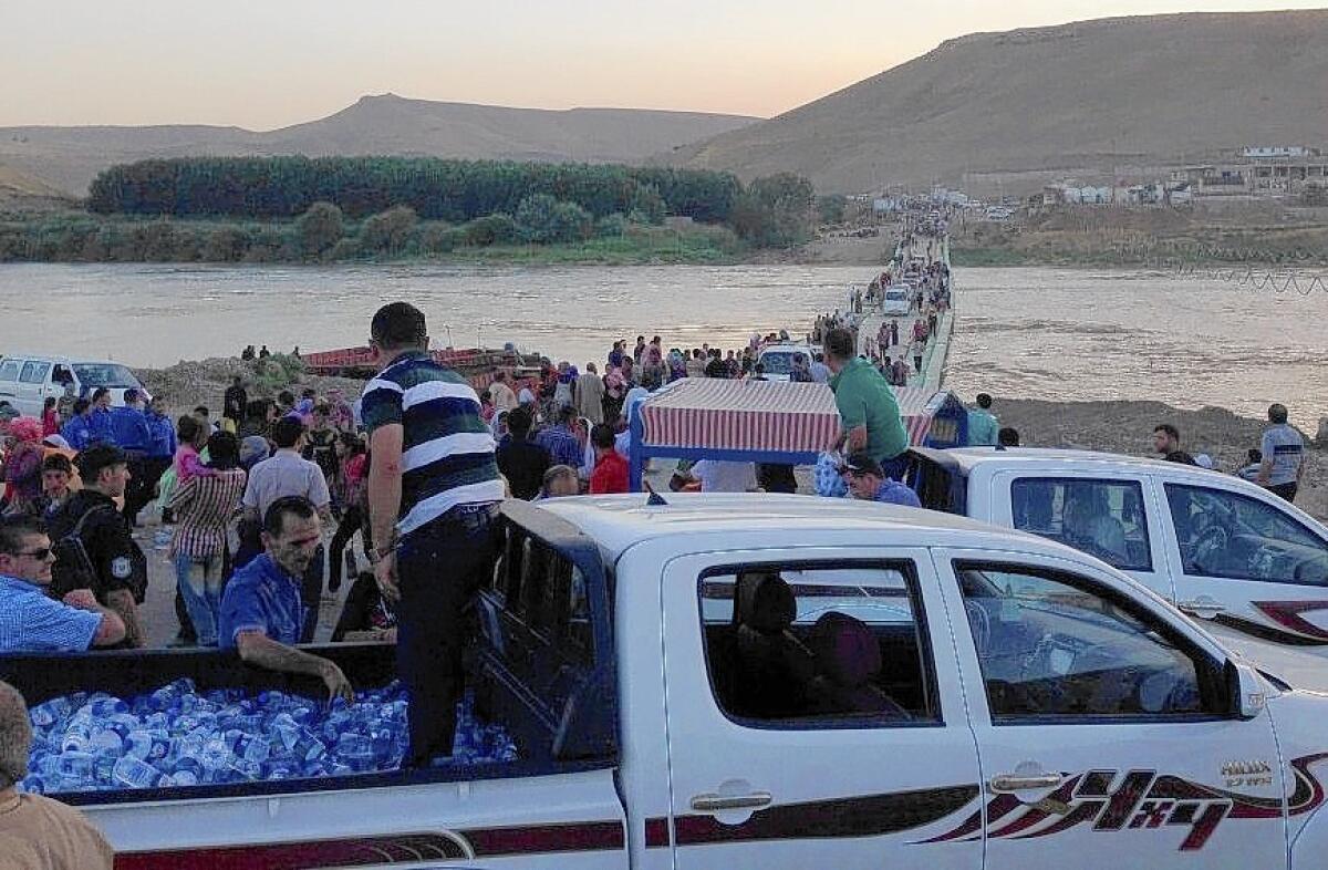 Iraqi Yazidis who fled Islamic militants several days ago cross the Tigris River from Syria into Iraq on Aug. 9, met by offerings of bottled water.
