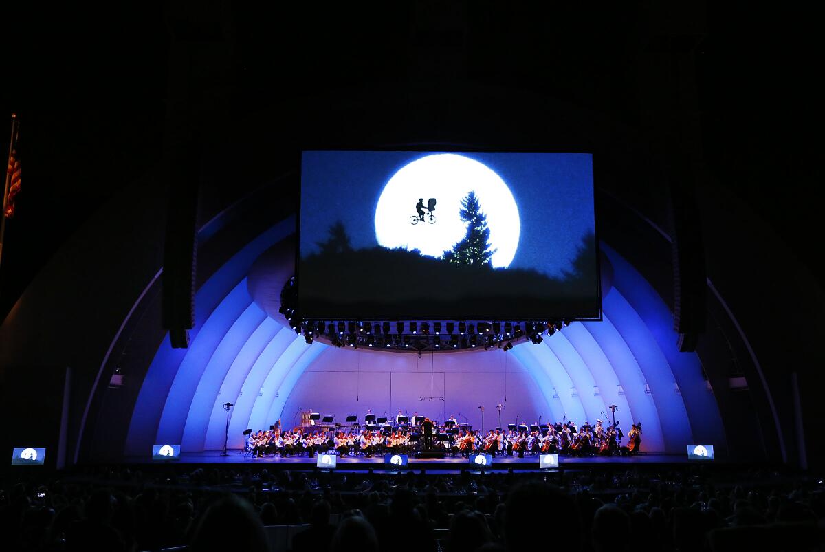 An outdoor amphitheater after dark with a large screen showing a large moon and the outline of a bike and two passengers.