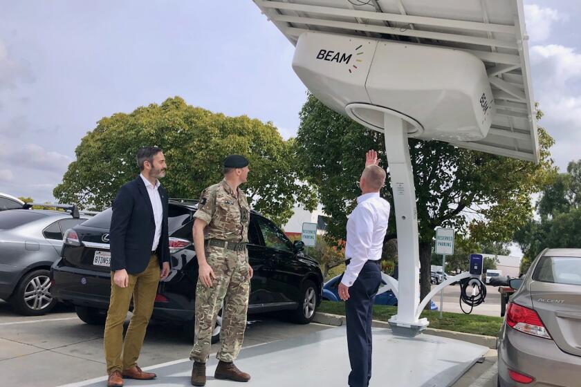 Beam Global CEO Desmond Wheatley (right) points to the top of an EV ARC transportable electric vehicle charging station  