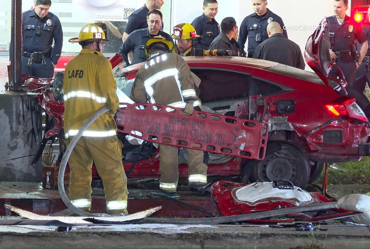 Firefighters carry a stretcher up to a crashed car with police officers standing nearby