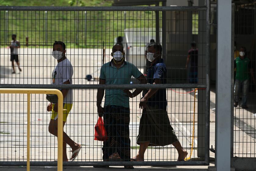 Foreign workers, wearing face masks as a preventive measure against the spread of the COVID-19 novel coronavirus, looks out from a fence of the workers' dormitory in Singapore on April 9, 2020. - Migrant workers in Singapore are living in fear following a surge of coronavirus infections in their dormitories where they say cramped and filthy conditions make social distancing impossible. (Photo by Roslan RAHMAN / AFP) / TO GO WITH Health-virus-Singapore-migration, FOCUS by Catherine Lai and Sam Reeves (Photo by ROSLAN RAHMAN/AFP via Getty Images)