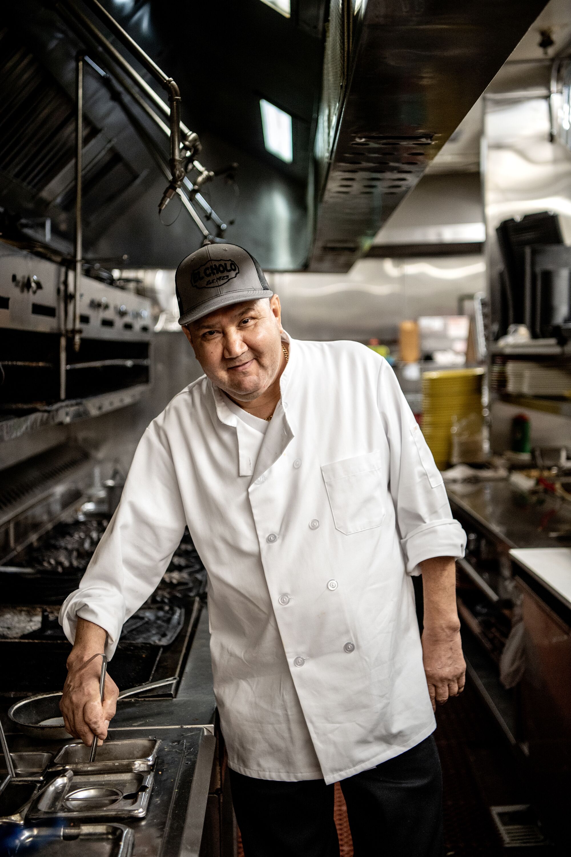 Moises Torres debout dans une cuisine, remuant quelque chose avec sa main droite tout en regardant la caméra.