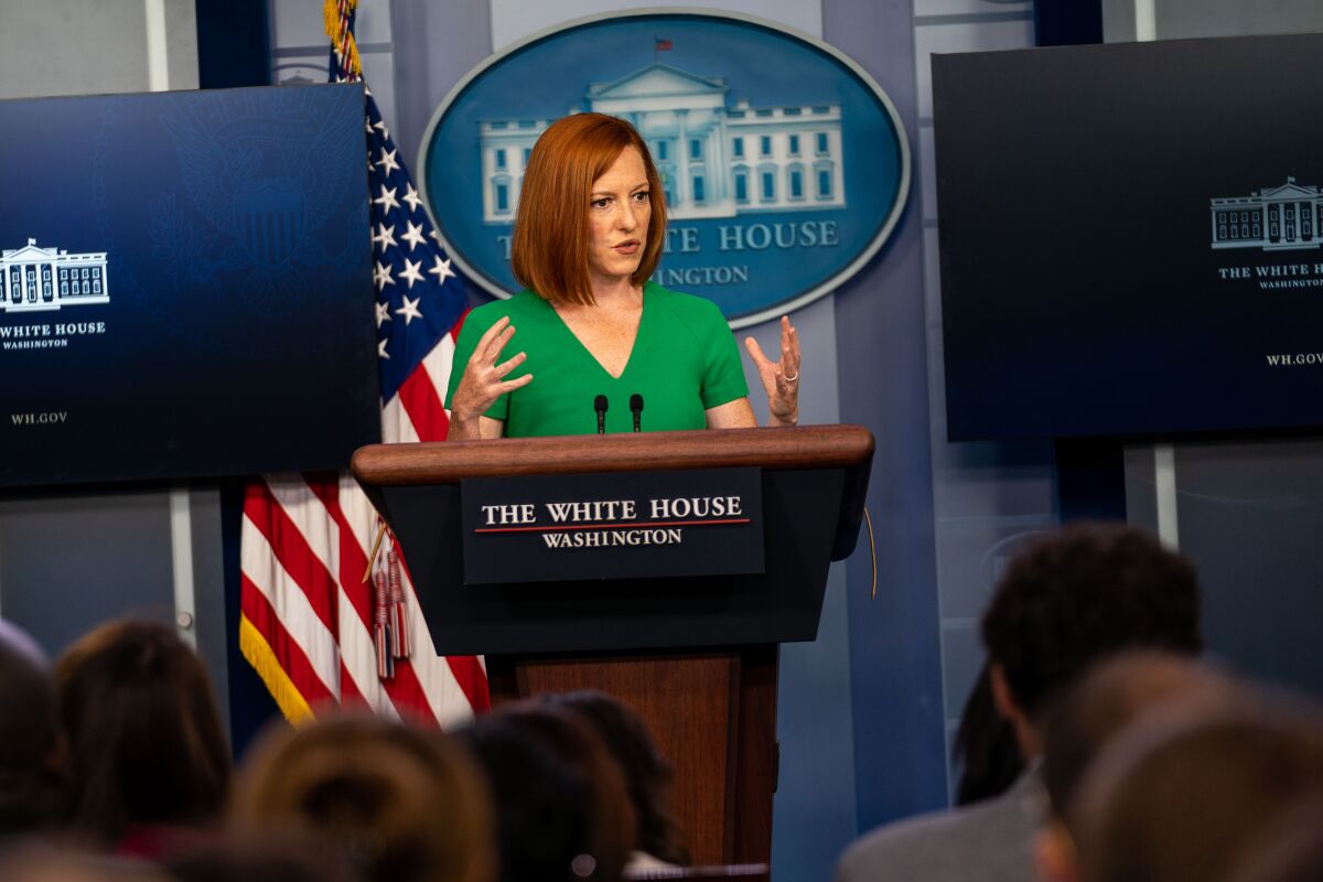 A red-haired woman in a green top gestures while speaking behind a podium at the White House.