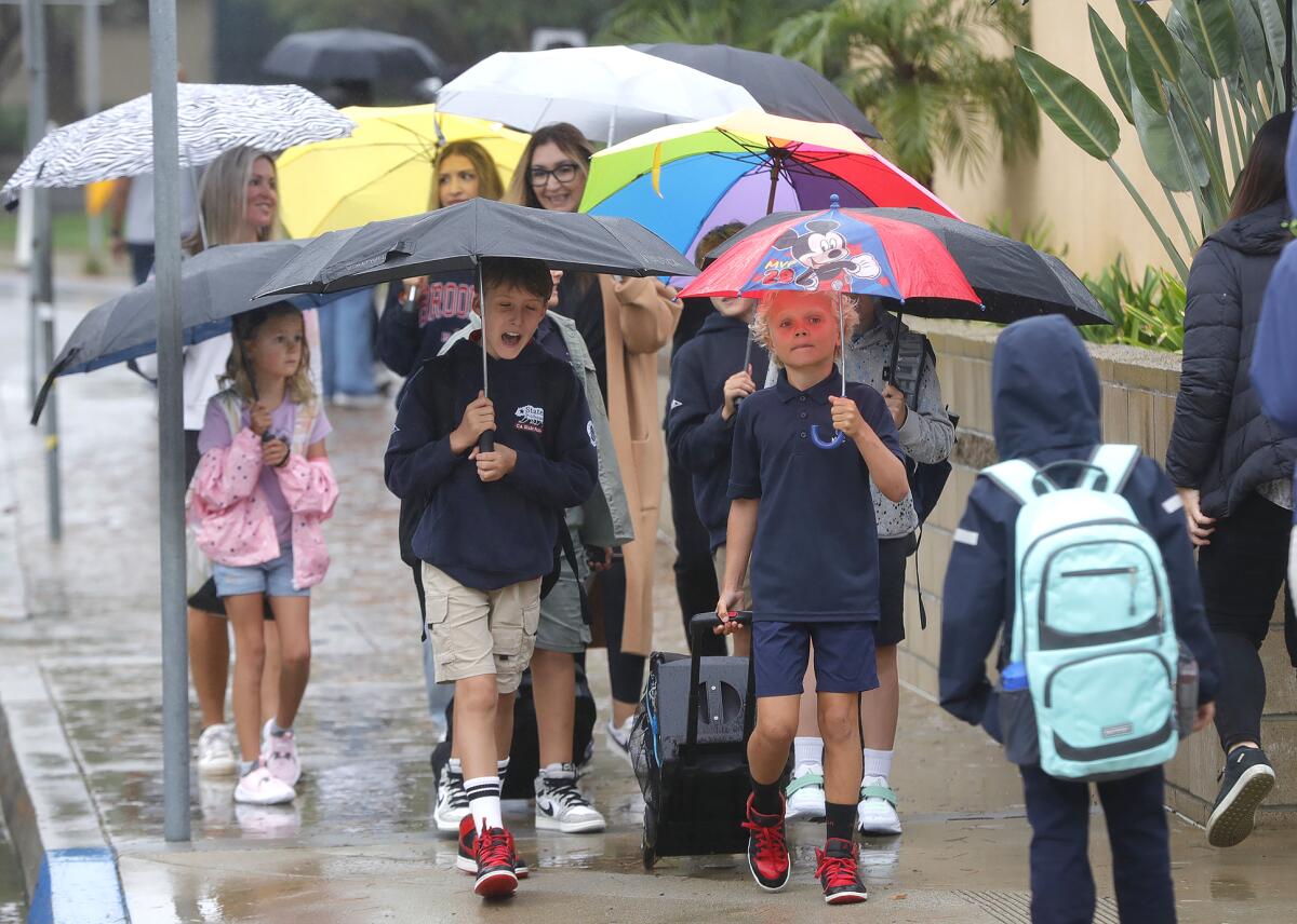 Kids accompanied by their parents arrive in rainfall for first day of school.