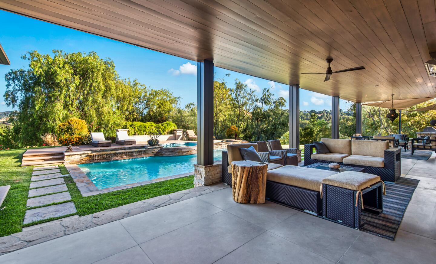 The patio has furniture, a pool nearby and trees in the background.