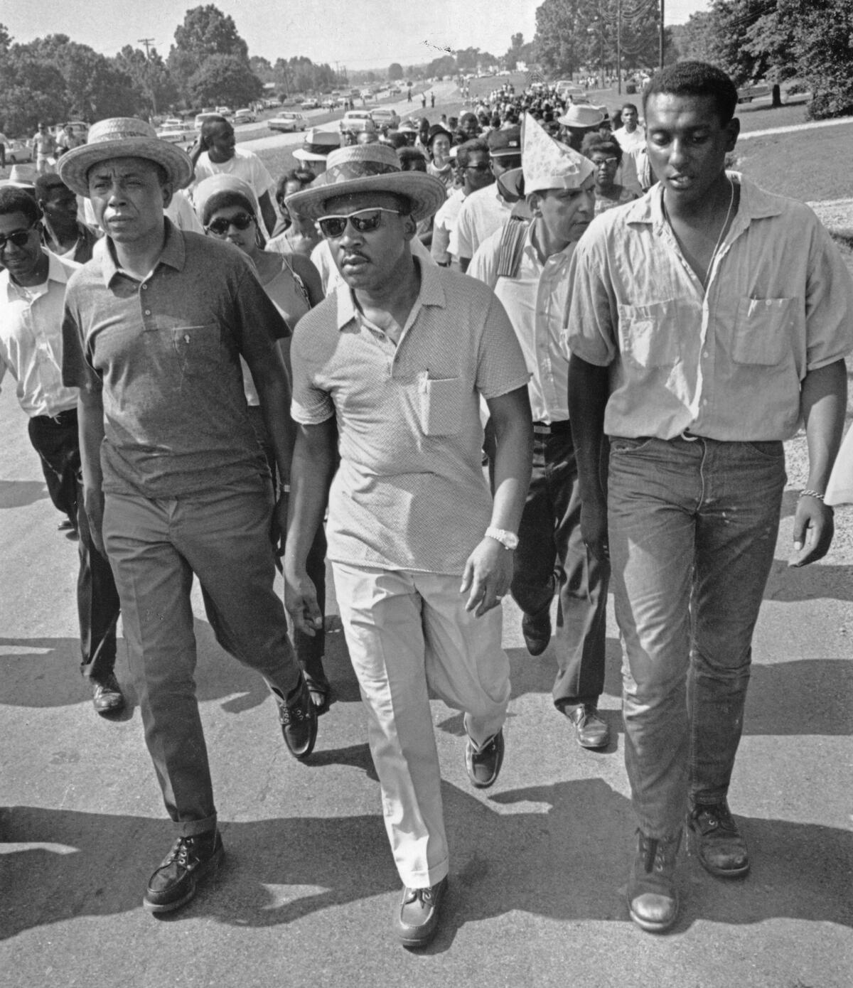 Three men wearing hats, leading a large march.