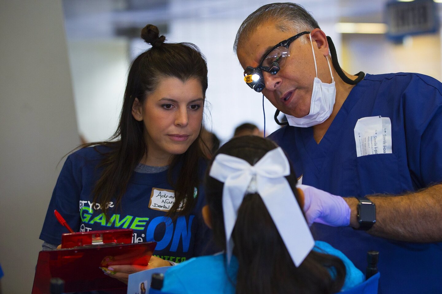 Dr. Mehran Raza and Adrian Nunes examine one of the 300 students that arrived to take part in the partnering of the San Diego Chargers and TeamSmile to provide a free dental clinic Tuesday at Qualcomm Stadium.
