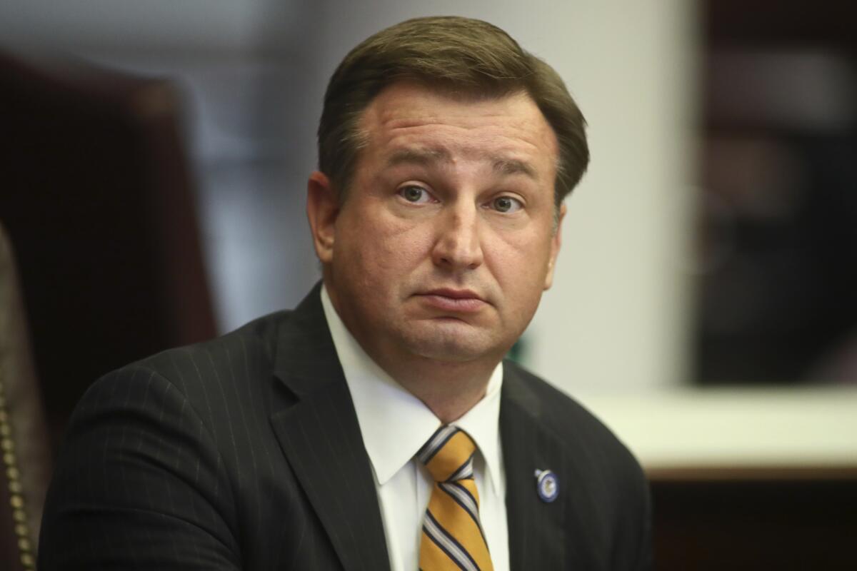 A man with dark hair, in a dark jacket and striped yellow tie 