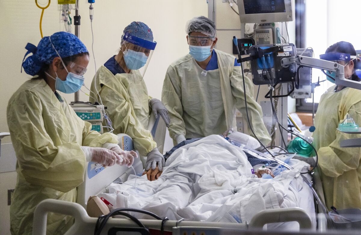Medical workers in protective gear surround a patient in a hospital bed.