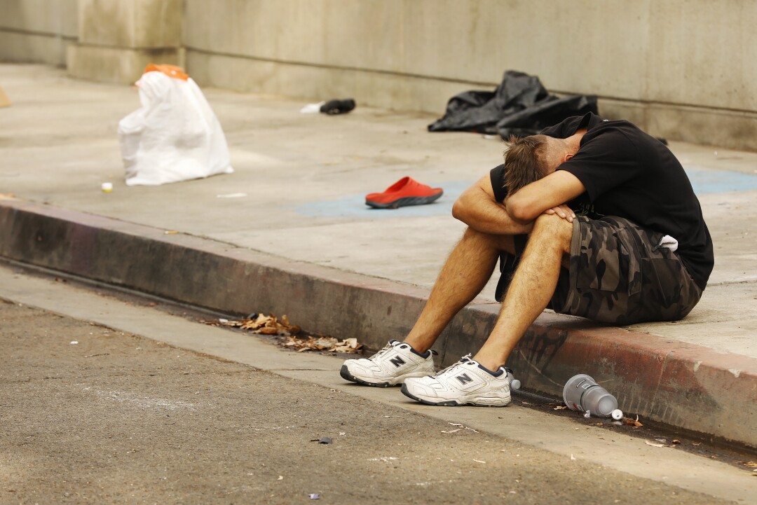 A man sits on a curb with his head down