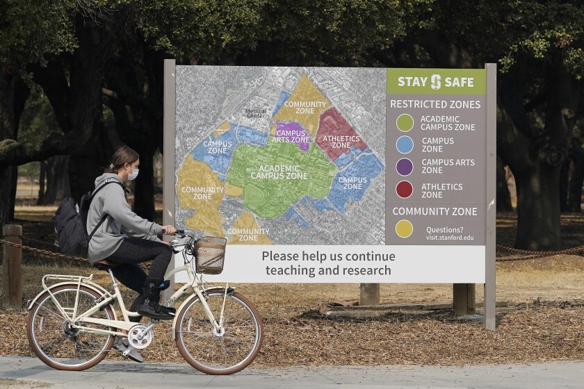 A bicyclist rides past a sign showing restricted zones around the Stanford University campus.