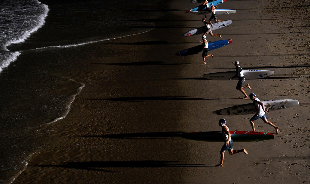 Competitors sprint to the water with paddle boards.