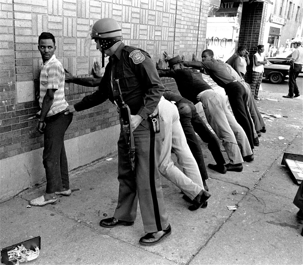 A police officer searches a youth as others are lined up against a wall.