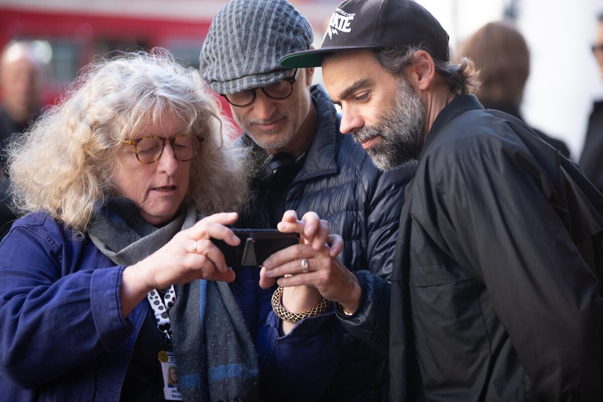 A woman and two men look at a electronic device.