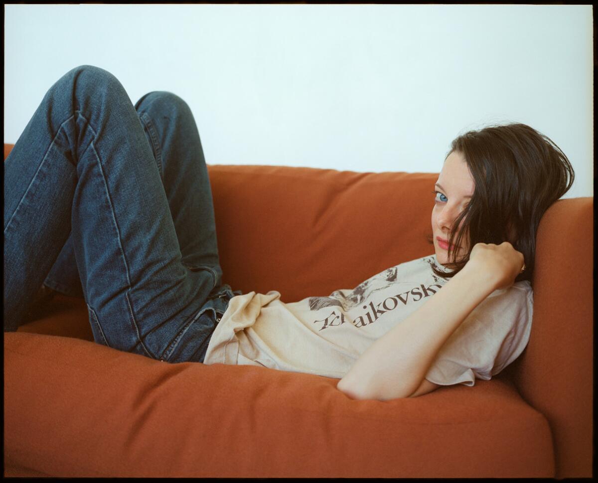 Rebecca Godfrey, in a T-shirt and jeans, lies on an orange couch.