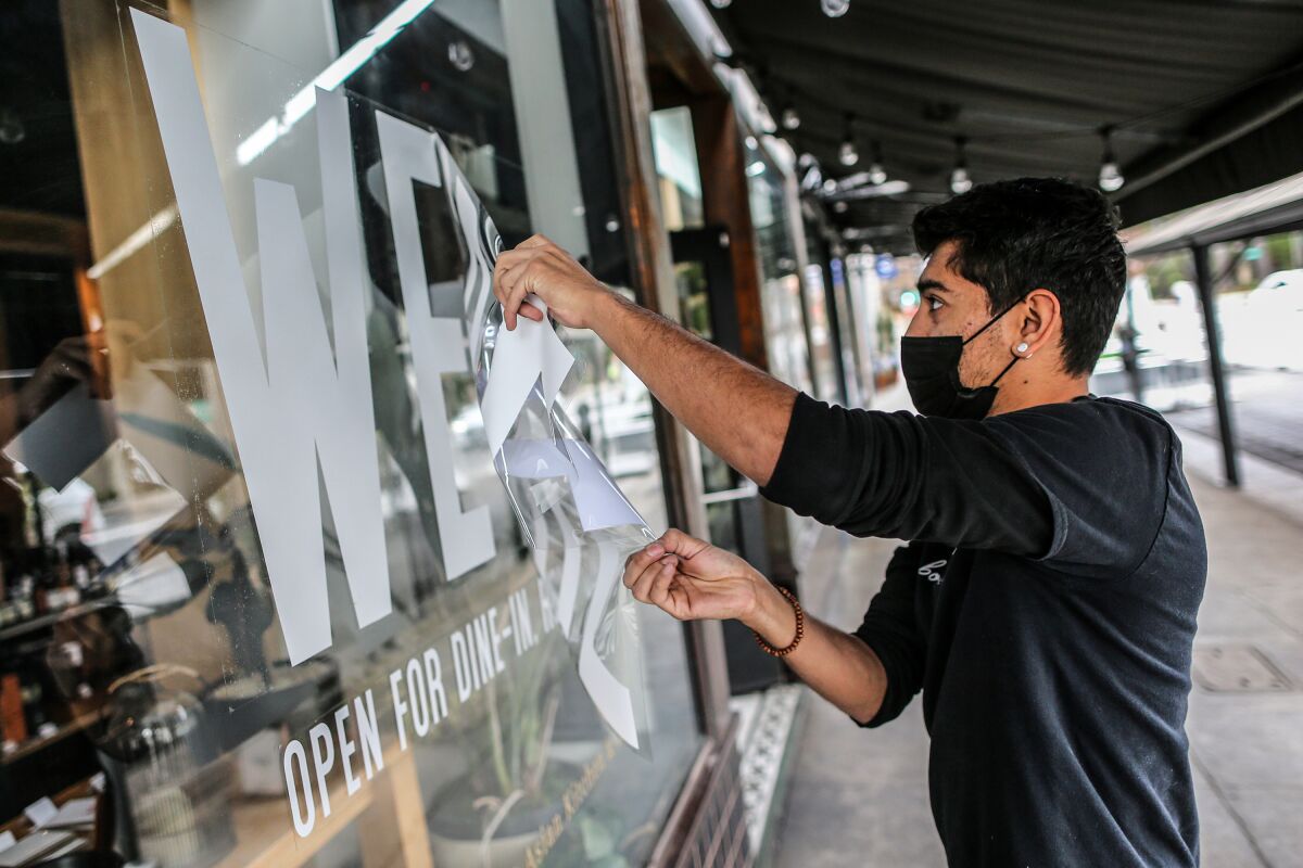 A masked restaurant employee peels a decal sticker off an exterior window