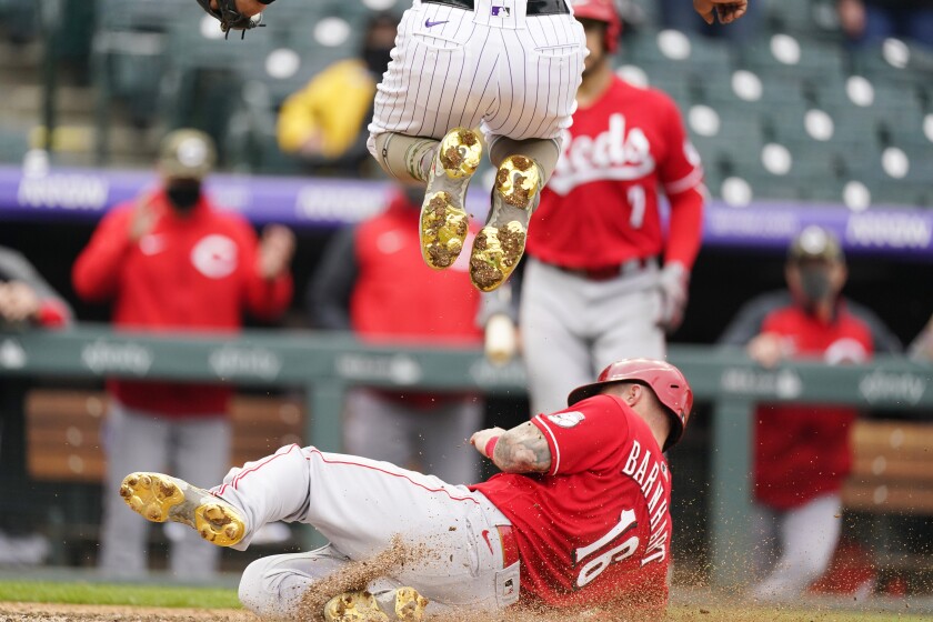 Cincinnati Reds' Tucker Barnhart, bottom, slides across home plate to score the tying run on a wild pitch by Colorado Rockies relief pitcher Mychal Givens, top, in the ninth inning of a baseball game Sunday, May 16, 2021, in Denver. (AP Photo/David Zalubowski)