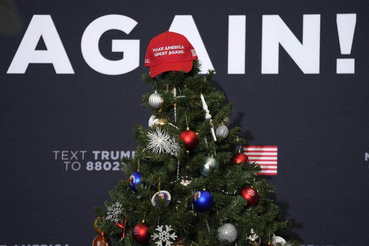 A Make America Great Again hat sits on top of a Christmas tree in front of a campaign sign at a Trump rally 