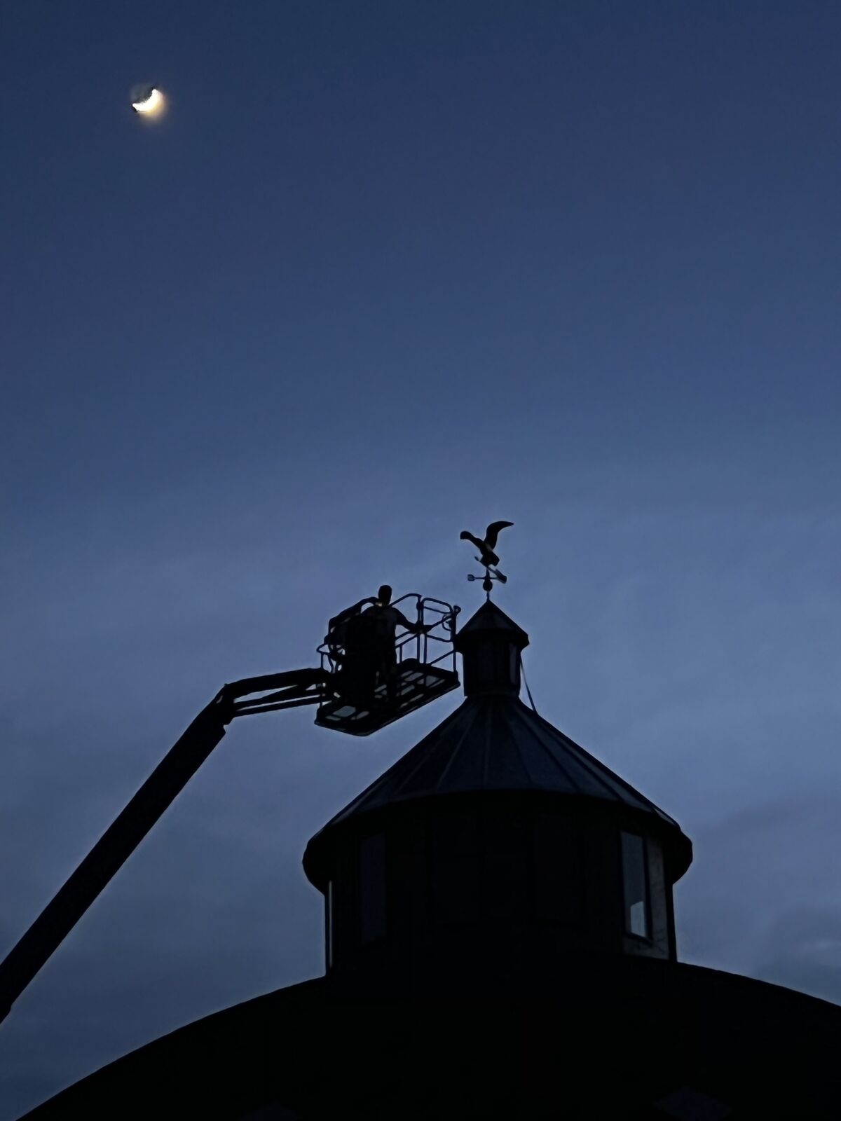 A person on a manlift near the top of a building, seen in silhouette 