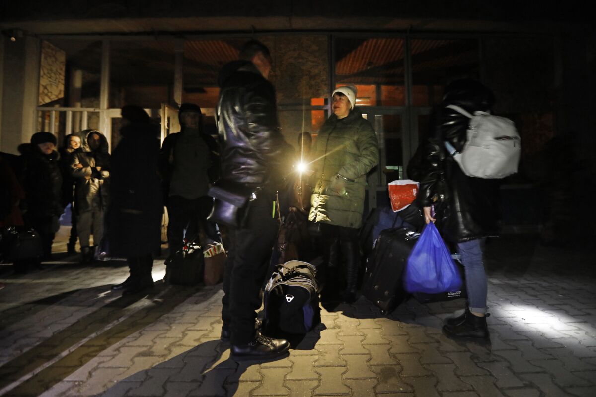 People stand with their luggage outside a dimly lighted building