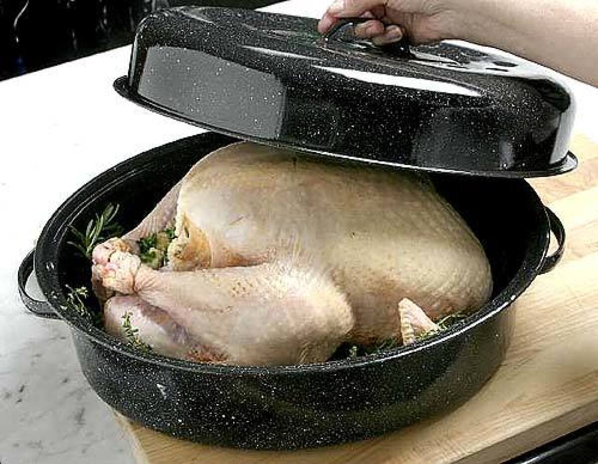 Putting turkey into granite roasting pan and covering.