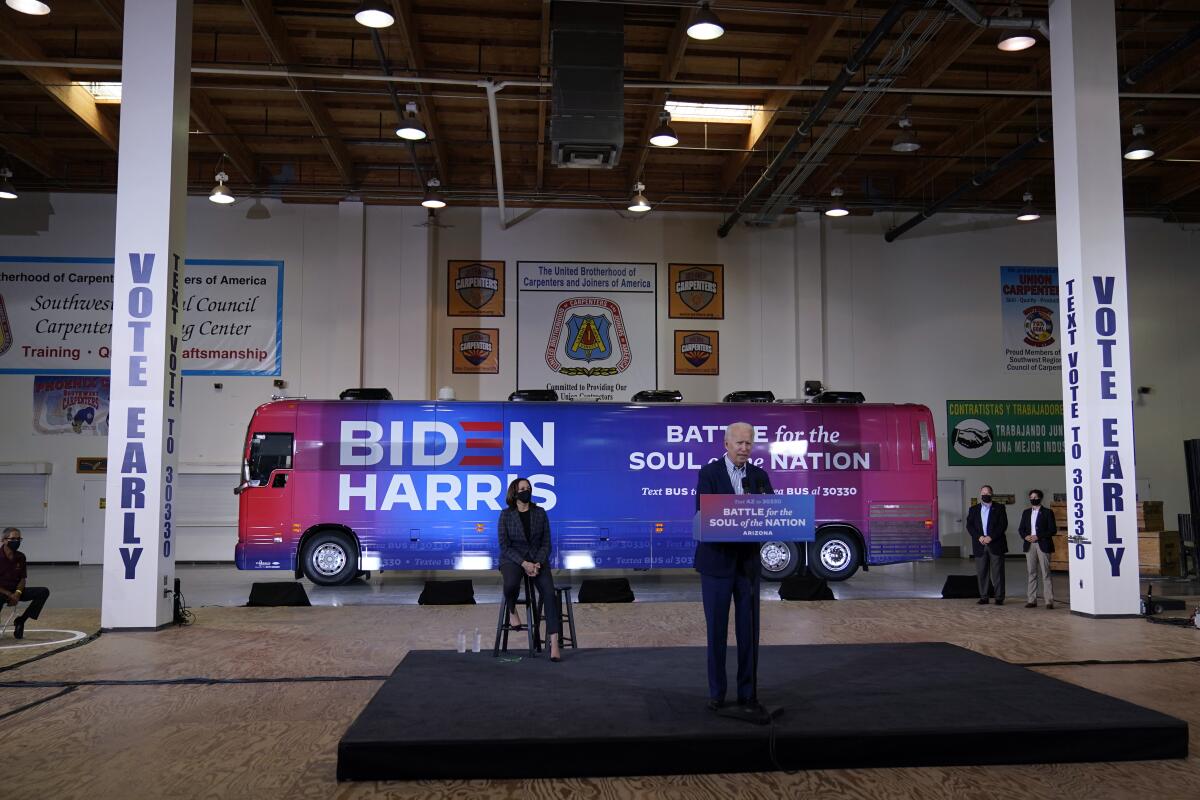 Joe Biden speaks on a small stage with Kamala Harris in front of their Biden-Harris campaign bus