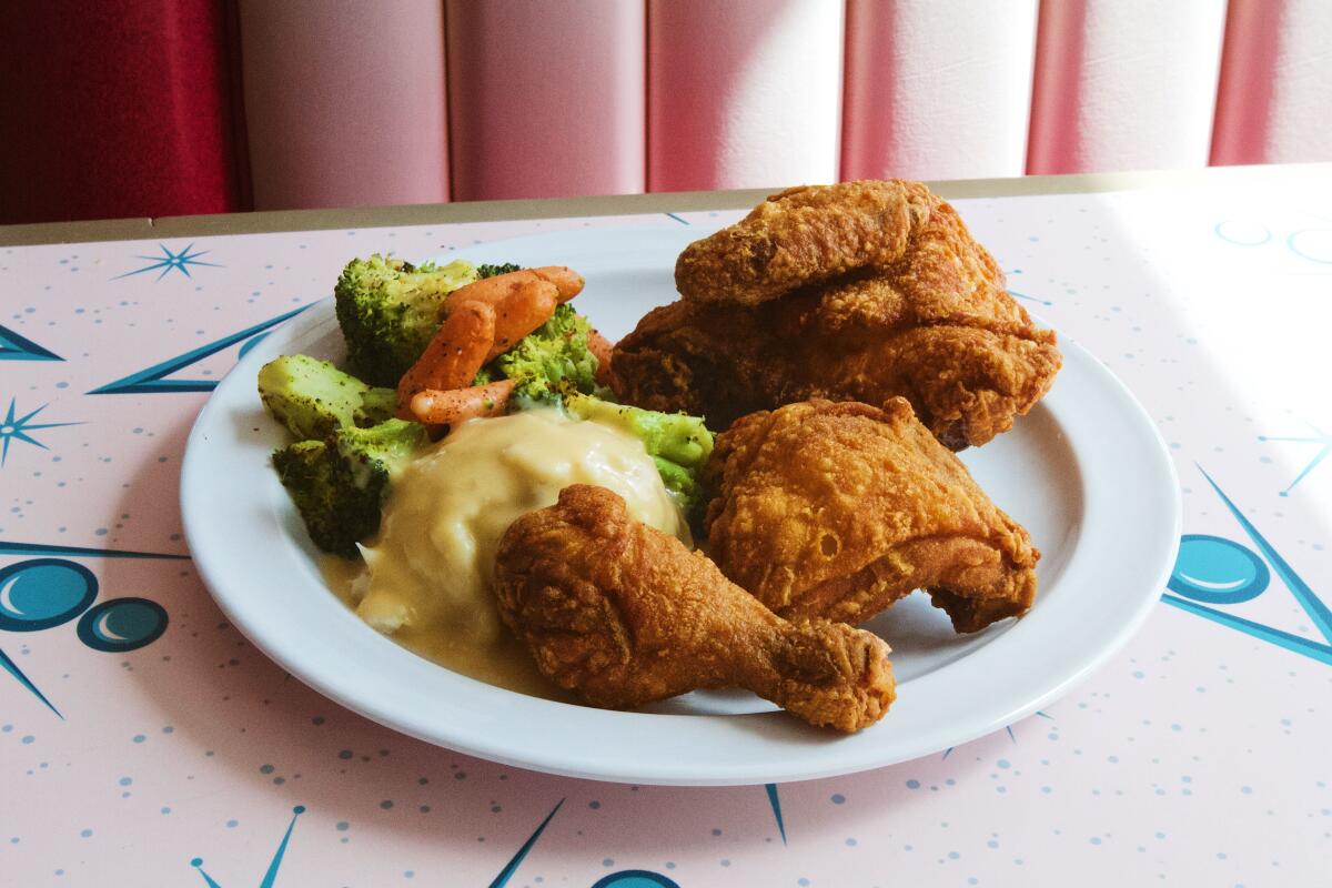 A plate of three pieces of fried chicken with mashed potatoes, gravy and vegetables