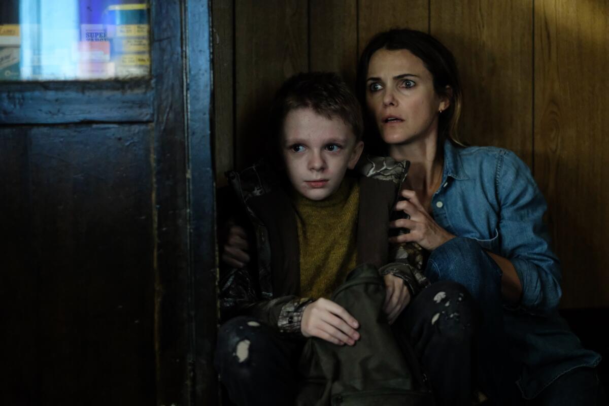 A woman and a boy crouch beside a door in the movie “Antlers.”