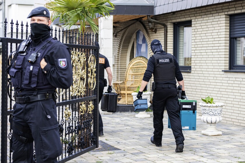 A police officer stands in front of a villa in Leverkusen, Germany, Tuesday, June 8, 2021. Special police units searched around 30 buildings in connection with money laundering and organized crime in the western German state of North Rhine-Westphalia. Investigators on Tuesday morning raided homes, offices and stores in Duisburg, Leverkusen, Gelsenkirchen and other cities. (Marcel Kusch/dpa via AP)