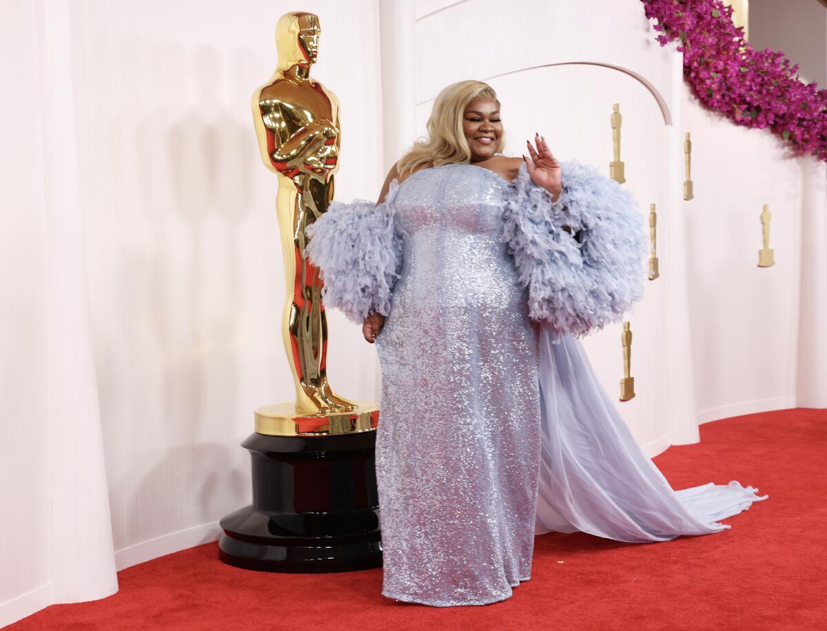 Da'Vine Joy Randolph, in a strapless, shimmering lavender gown with feathered sleeves and train, poses on the red carpet.