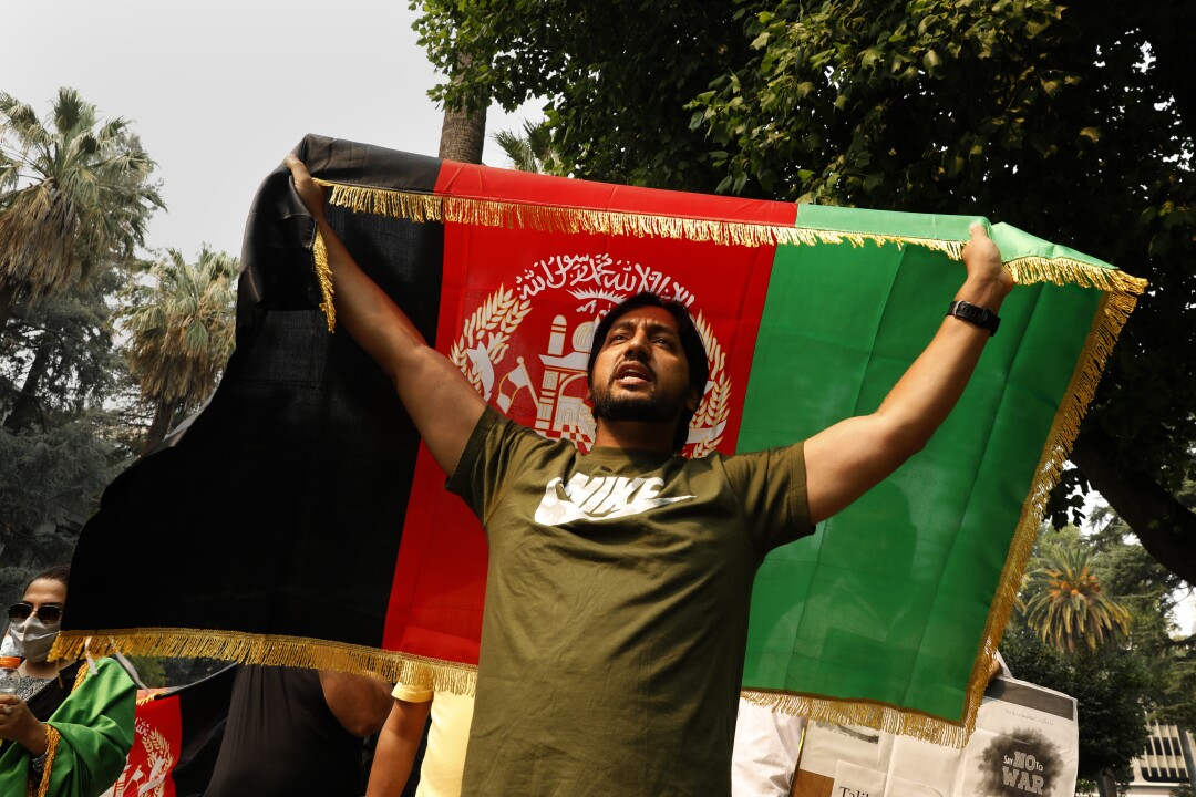A man with arms outstretched holds an Afghan national flag