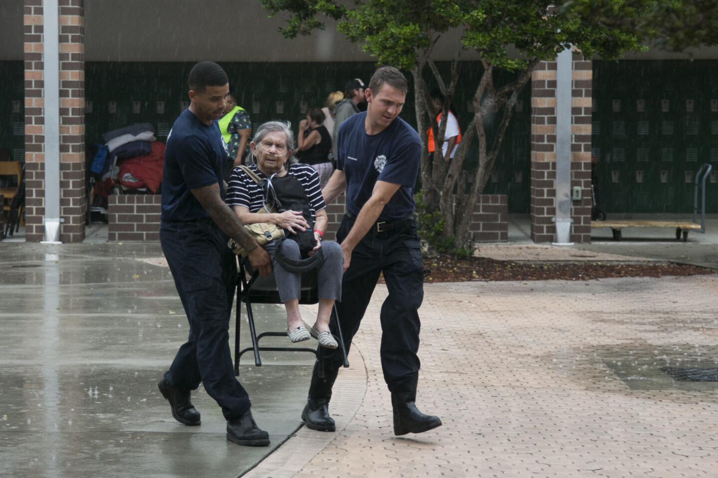 Firefighters Dohnovan Simpson, from left, and Jacob McGovern carry Dolores Gevaza, 83, across the courtyard in the rain at John Hopkins Middle School on Sept. 10, 2017, in St. Petersburg, Fla. The school filled classrooms and hallways with people evacuating.
