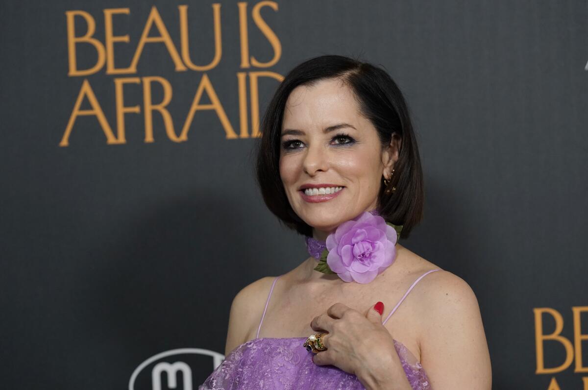 Parker Posey poses in front of a backdrop with the words "Beau Is Afraid" on it.