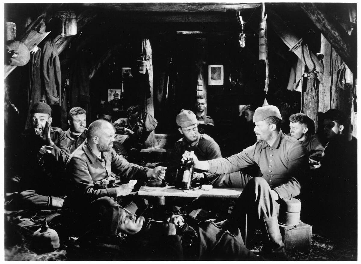 German soldiers in a shelter in play cards and drink at a low table in “All Quiet On The Western Front” (1930)
