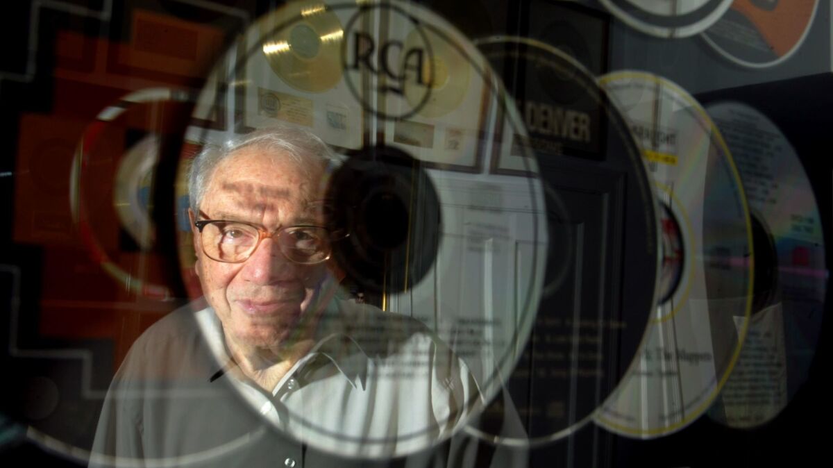 Milt Okun, founder of Cherry Lane Music Group, reflected in the framed CDs of John Denver, one of the many recording artists he shaped.
