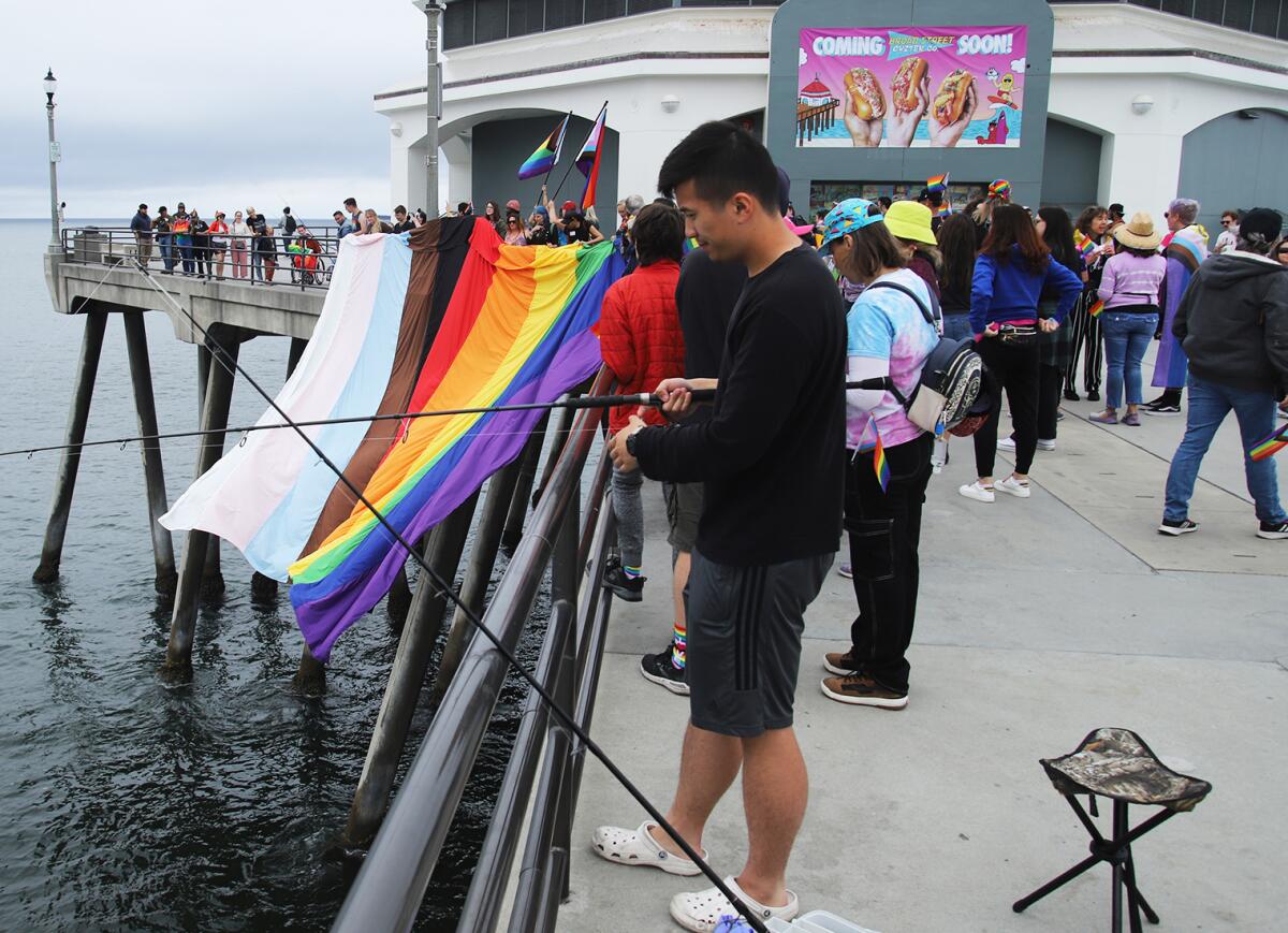 A fisherman at the side of the Huntington Beach pier as local activists and LGBTQ+ supporters hang a Pride flag Sunday.