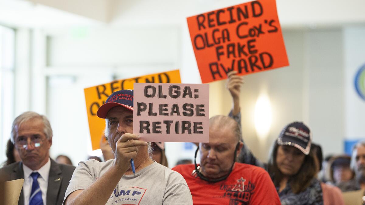 Protesters hold up signs during the Coast Community College District board meeting.