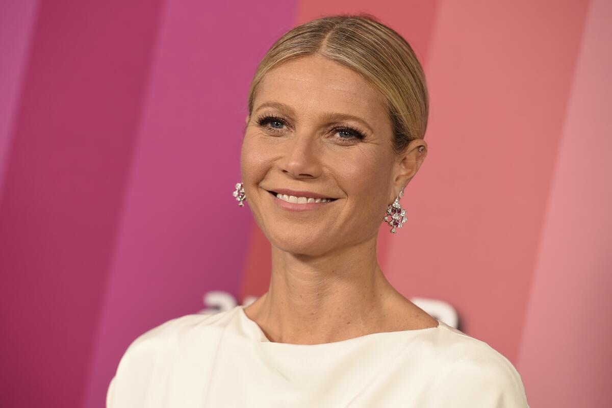 A smiling blond woman with her hair pulled back, at a red carpet event in L.A., wearing white  and earrings. 