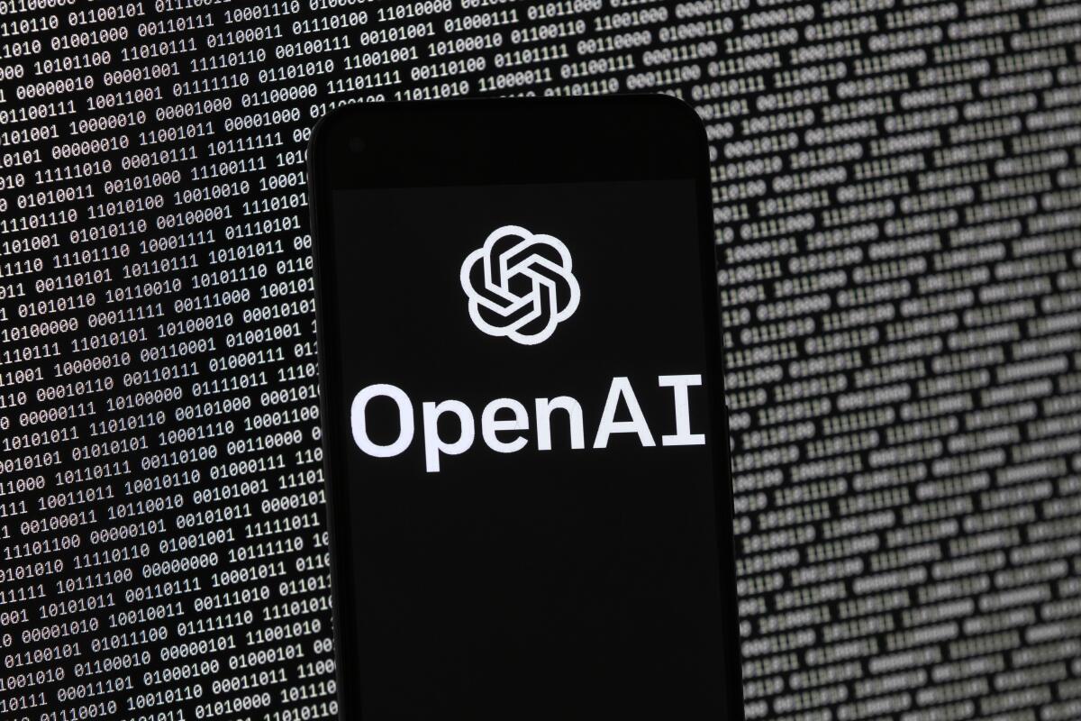 The OpenAI logo appears on a mobile phone in front of a computer screen with random binary data.