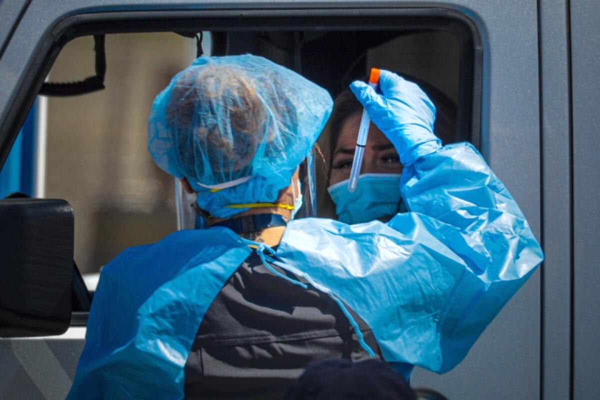 A San Bernardino County healthcare worker collects a sample at a drive-through coronavirus testing site in Victorville.