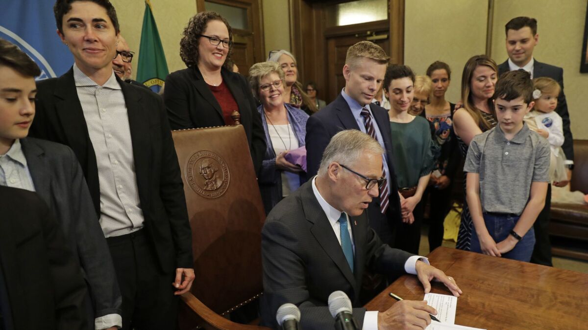 Katrina Spade, second from left, the founder and chief executive of Recompose, a company that hopes to use composting as an alternative to burying or cremating human remains, looks on Tuesday as Washington Gov. Jay Inslee signs a bill into law allowing "human composting."