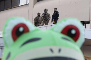 Law enforcement officers watch from a ledge as a protester stands outside in an inflatable frog costume