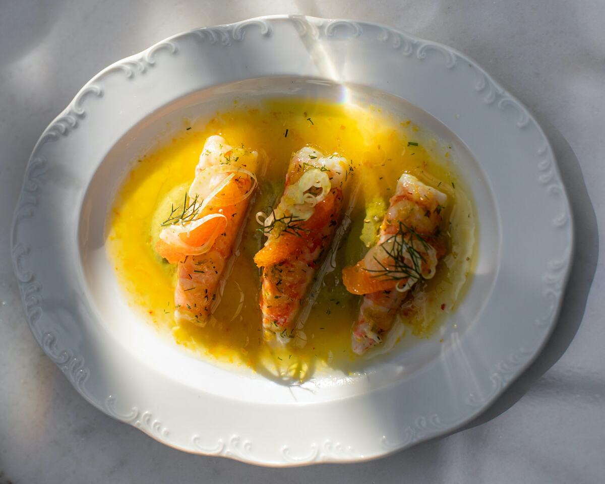 An overhead photo of three shrimp dressed with citrus and fennel on a white oval plate.