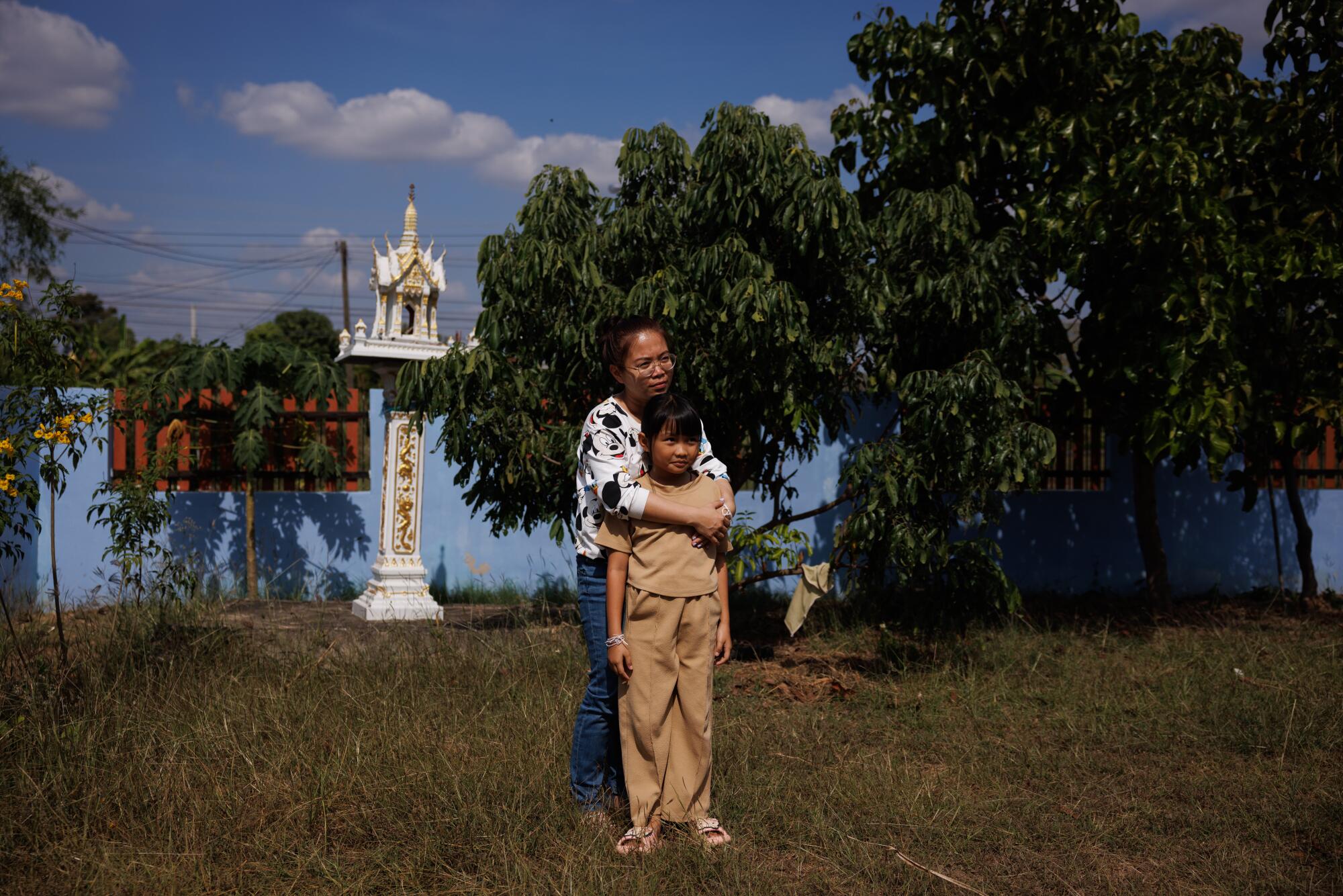 A woman and daughter pose for a portrait on a lawn in Thailand.