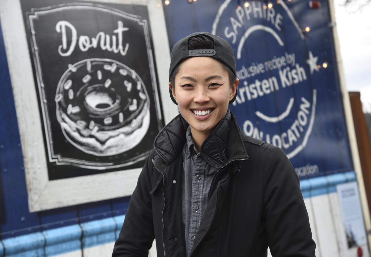 "Top Chef" winner Kristen Kish poses in front of a food truck wearing a backwards cap and a layered jacket
