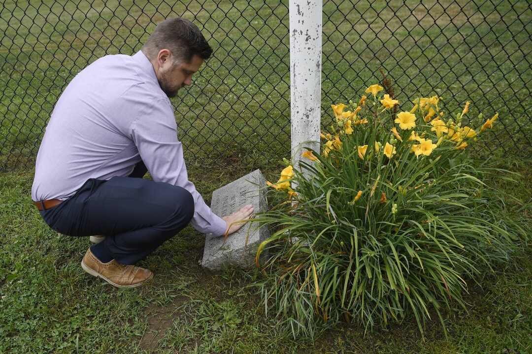 Brett Eagleson wipes grass off a memorial stone for his father at a baseball field