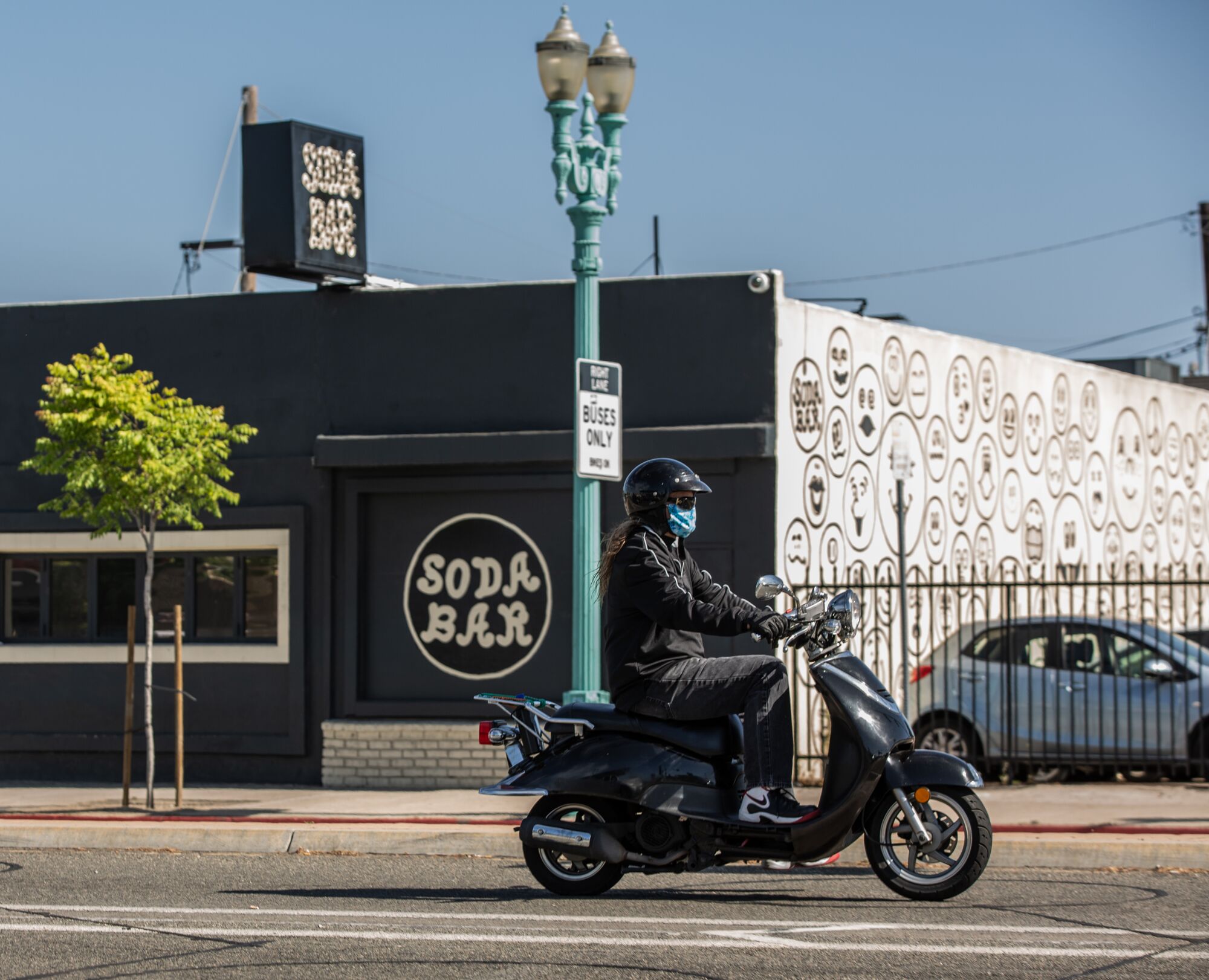 A moped rider wearing a mask drives past Soda Bar in City Heights, one of the many music venues that will be closed for the foreseeable future due to COVID-19 on May 14, 2020 in San Diego, California.