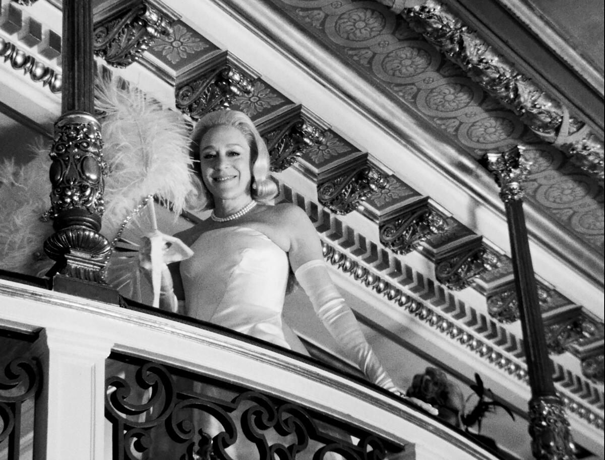 A woman in a ballgown and long gloves looks down from an opulent balcony in "Feud."