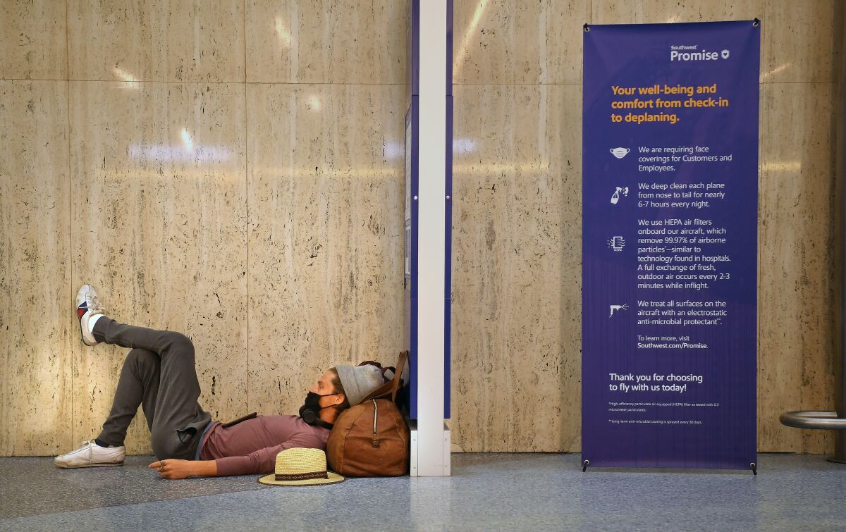 A traveler sleeps at LAX next to a sign describing the airport's COVID cleaning protocols.