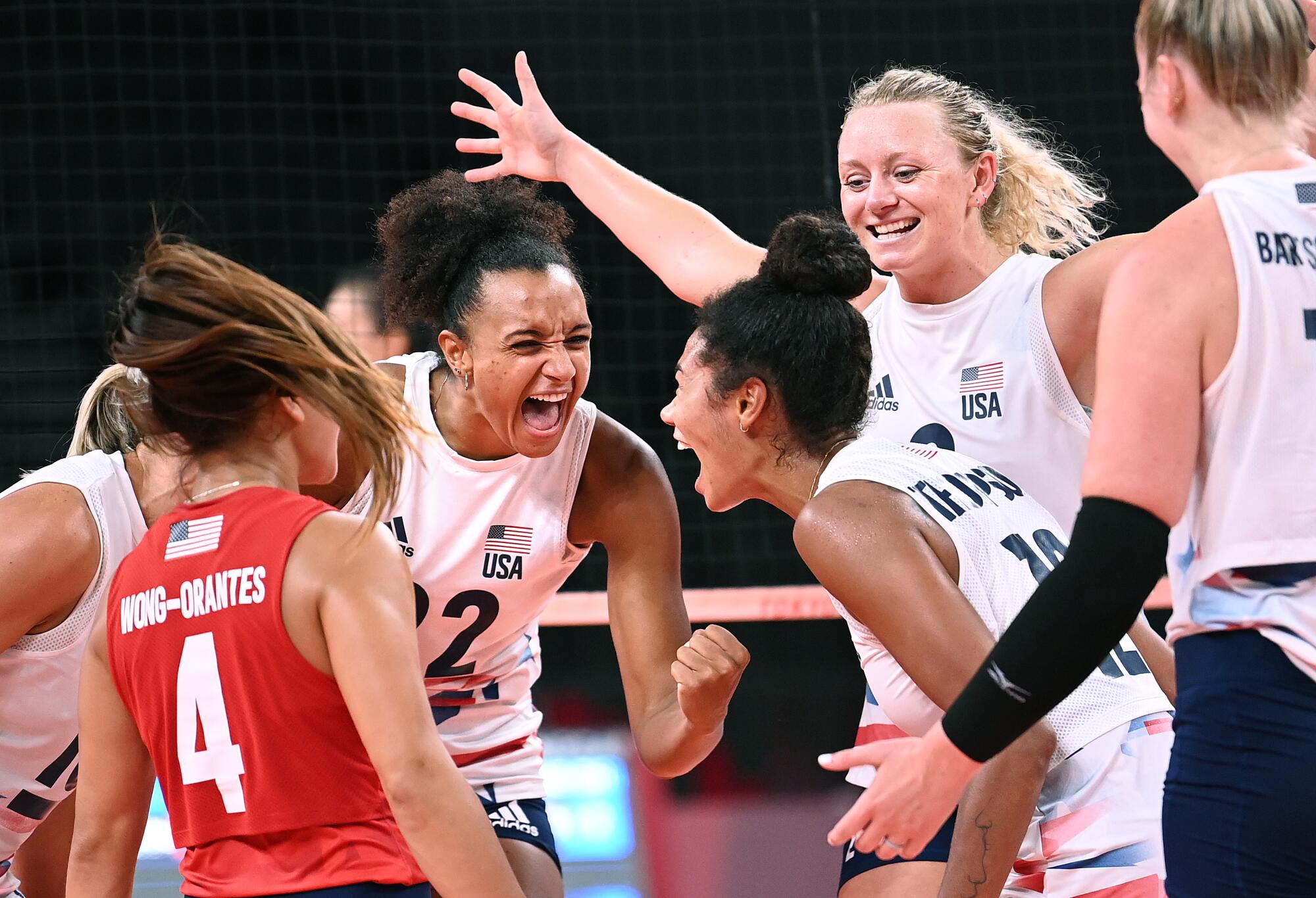 Women on the volleyball court smile, stretch out their arms and shout.